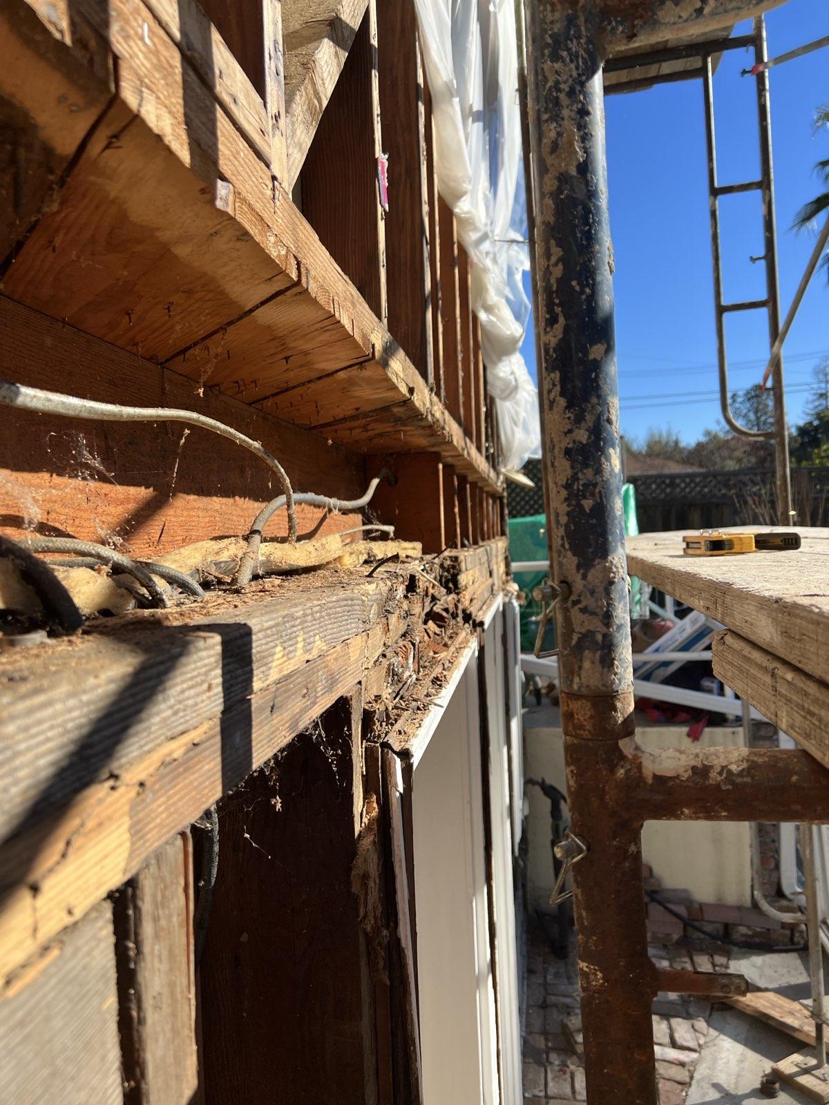Close-up of rotted bay window joists exposed during demolition — debris, water damage, and decayed framing visible inside the structural cavity